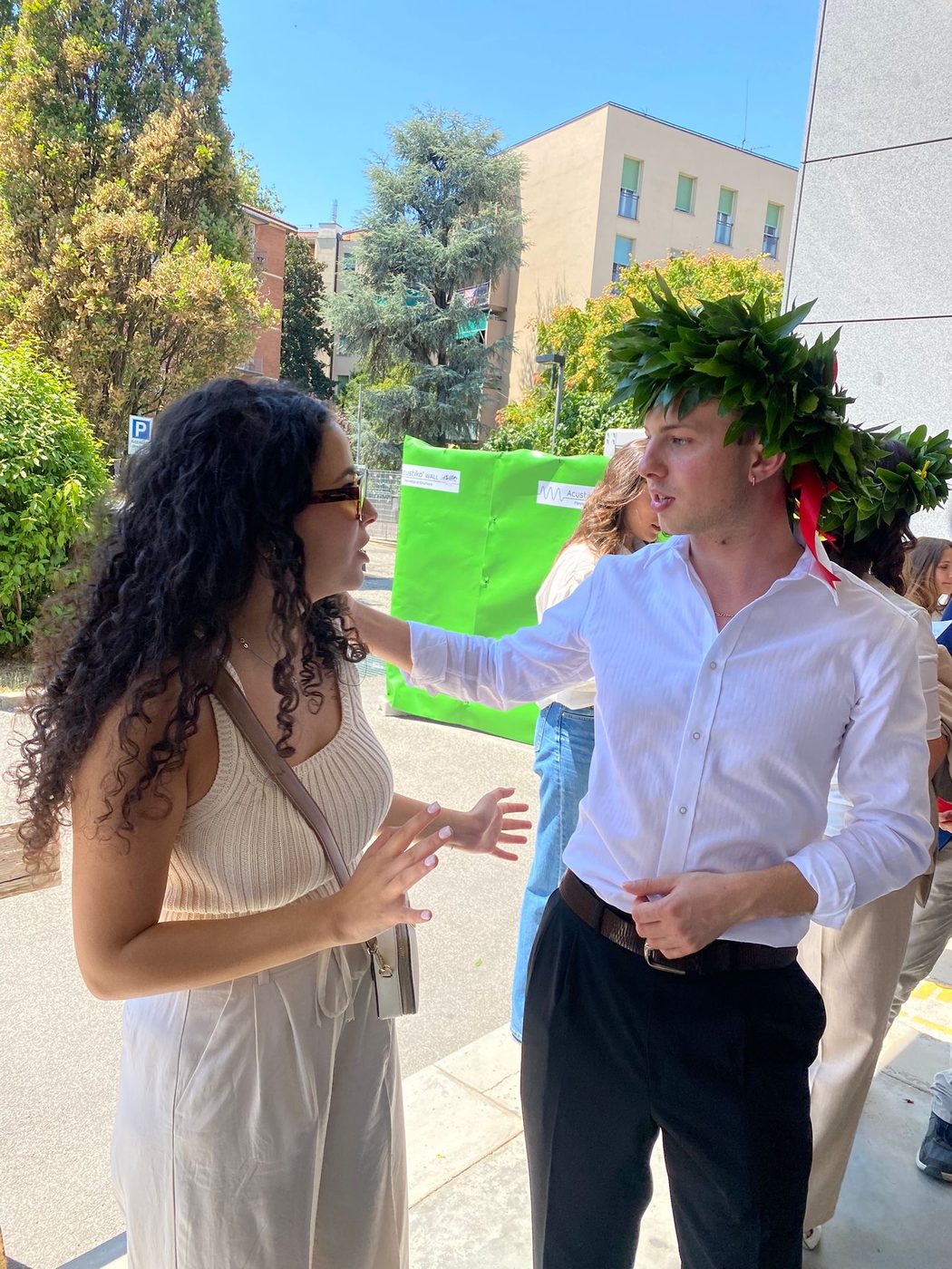 Alessio wearing a laurel wreath on graduation day, mid-conversation with a friend outside the university.